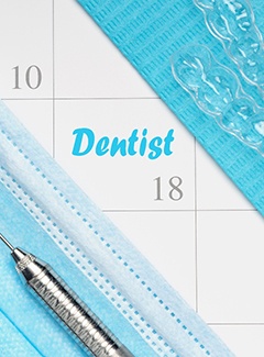 A calendar that shows the date and the word “dentist” along with a mask, Invisalign aligners, and dental instruments