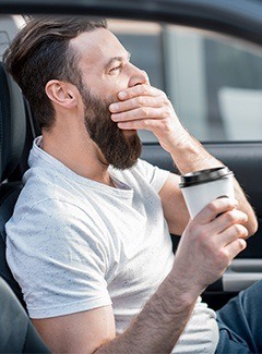 man yawning with coffee in hand