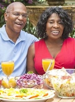 couple sitting at a table outside with various foods and beverages