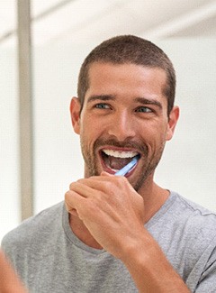 Man smiling while brushing his teeth in bathroom