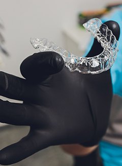 A dental professional wearing a black glove and holding an Invisalign aligner in preparation to put it in a patient’s mouth