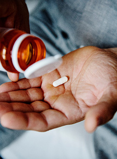 a person taking holding a prescription bottle with a pill in their hand