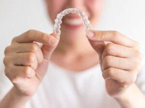 Smiling patient without bruxism holding out Invisalign aligner