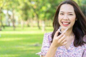 Young woman standing outside, holding Invisalign aligner