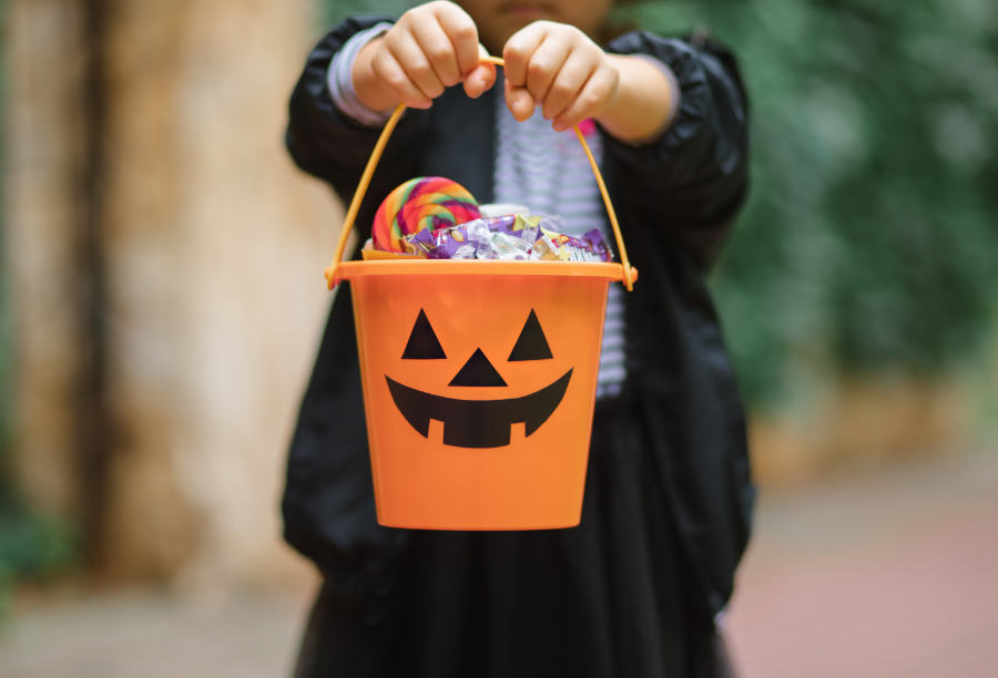 Child holding plastic pumpkin with Halloween candy